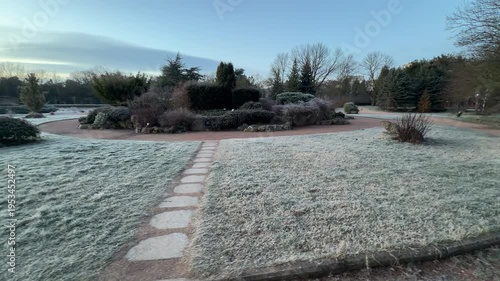 Wallpaper Mural A line of flat stones crosses a frost-covered lawn toward a circular garden bed. Evergreen trees and bushes stand still under a pale morning sky. The atmosphere is crisp, organized, and serene. Torontodigital.ca
