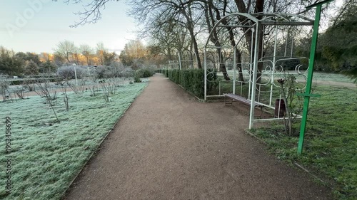 Wallpaper Mural Elegant white metal arches stand over a quiet bench along a gravel walkway. The frost-covered grass and dormant bushes create a cold, nostalgic atmosphere in this peaceful park setting. Torontodigital.ca