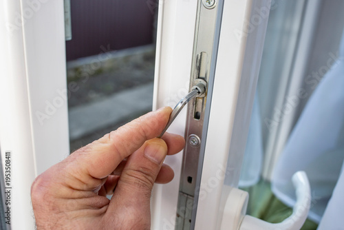 Locksmith opened and adjusting for winter with a screwdriver the lock mechanism of the plastic PVC window in the house. Installation, configuration and maintenance of plastic windows.