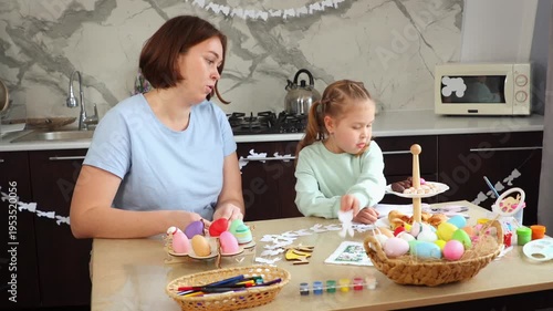 Mid shot of mother and daughter are preparing for the Easter holiday together. Little girl and a Caucasian woman decorate the room