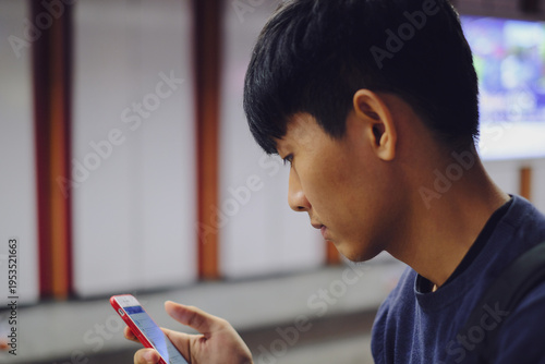 Young Asian Man Using Smartphone in Subway Station with Blurred Background