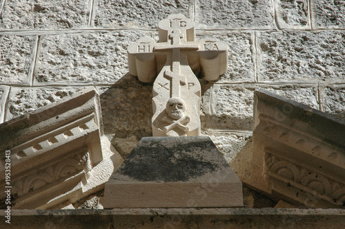 Obraz na plátně An ornate stone cross with a skull and crossbones memento mori symbol is mounted