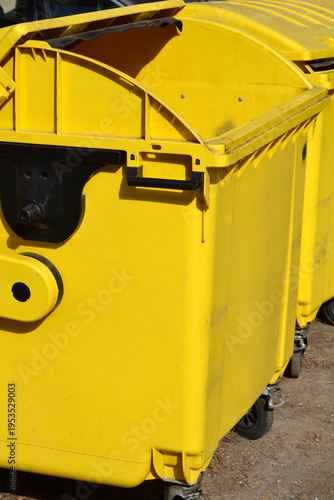 Row of bright yellow industrial plastic waste containers with wheels and open lids standing outdoors on a sunny day