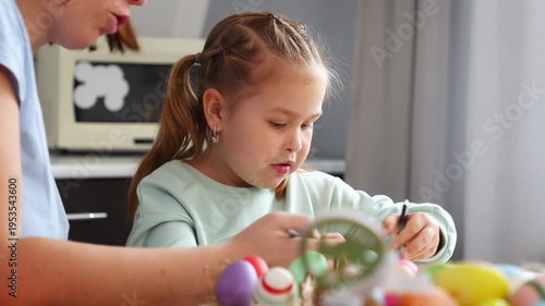 Close up of teacher and little cute daughter are engaged in children's creativity together, drawing Easter decorations, sitting at the table