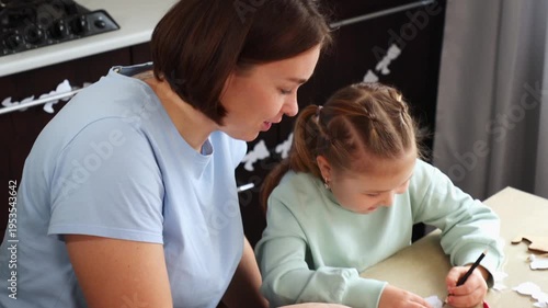 Close up of teacher and little cute daughter are engaged in children's creativity together, drawing Easter decorations, sitting at the table. Top view
