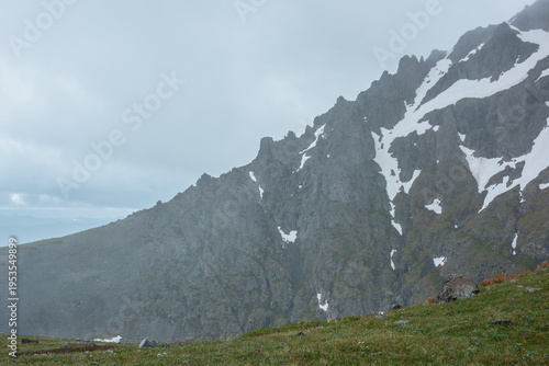 Minimal alpine view from grassy pass above abyss to sharp rocky ridge with sn...