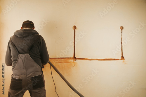 Konstfotografi A worker using a wall chaser machine to cut grooves in a wall for electrical installations