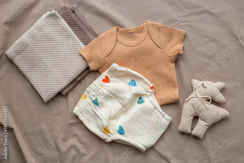 Beige baby bodysuit and white cotton diaper pantie and towels on on beige sheet, top view. Eco friendly cloth and accessories