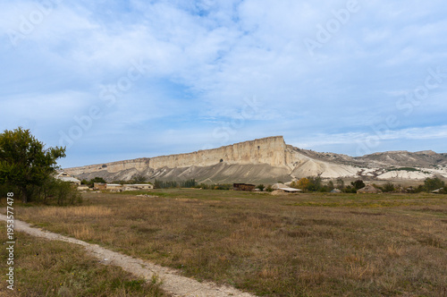 Impressive landscape with towering white cliffs covered in erosional patterns. Green vegetation in foreground contrasts with light-colored rock formations. Landscape showcases pristine beauty.
