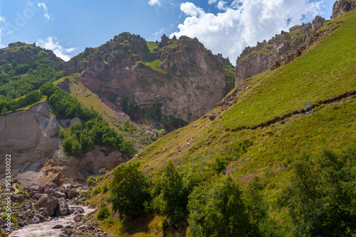 Quadro em tela Rocky mountain valley with cave openings, green slopes and hikers