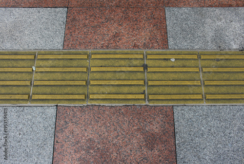 Close up of grey and red pavement with yellow tactile tiles. Yellow tactile paving on walkway, guiding block for blind and visually impaired.