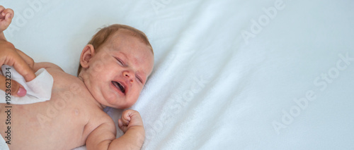 Obraz na plátne Crying newborn baby lying on white bed, concept of infant colic and discomfort