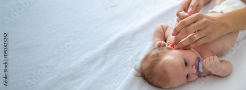 Mother cleaning baby's ears with cotton swab, concept of infant hygiene and daily care.