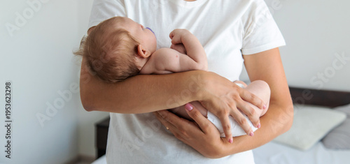 Young mother cradling newborn baby in her arms at bright bedroom, care concept.