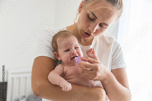 Mother giving pacifier to crying newborn baby, concept of soothing and infant care.