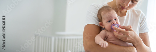 Mother giving pacifier to crying newborn baby, concept of soothing and infant care.