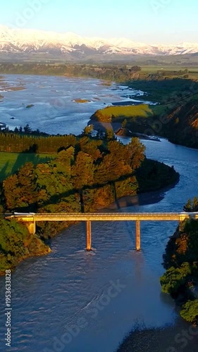 4K Vertical Aerial River Bridge Over Lush Valley with Snowy Mountains at Golden Hour
