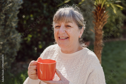 Mature woman smiling and holding mug outdoors in sunlight