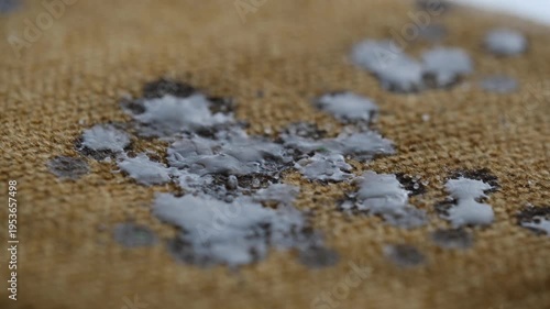 White candle dripping wax on to cloth or furniture upholstery on a brown background, at a cozy location. Concept of everyday life problem and home cleaning