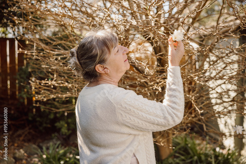 Mature woman holding magnolia flower and smiling in sunny garden