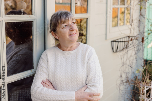 Mature woman looking away thoughtfully while standing by house outdoors