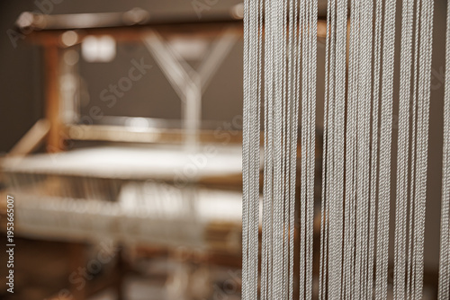 Close-up of vertical loom threads in sharp focus with a blurred weaving machine in the background, highlighting textile craftsmanship and pattern creation