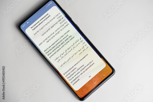 Israel emergency rocket alert notification on phone screen in Hebrew, English, Arabic and Russian, advising to go to shelter and stay in protected space. War and civil defense concept.