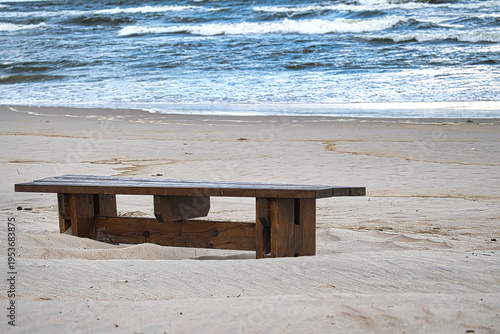 Weathered wooden bench sits alone on a sandy beach overlooking the ocean waves