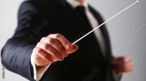 Close-up of a conductor's hand holding a baton, guiding an orchestra, symbolizing leadership and musical direction.