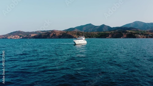 Large White Yacht on Blue Sea with Rocky Hills and Coastal Village in Background