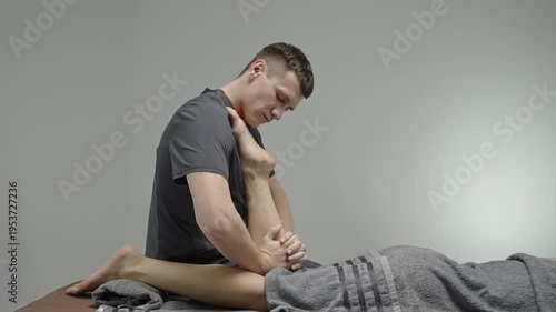 Professional massage therapist performing targeted leg stretch and deep tissue techniques on client lying prone on table, focusing on hamstring mobility, relaxation and bodywork.