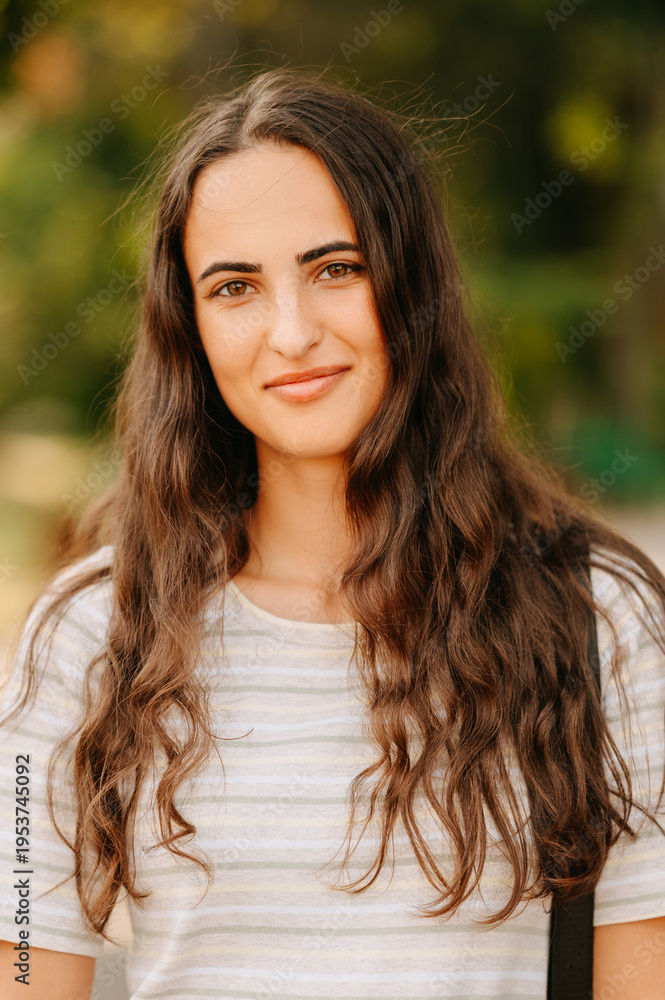 Obraz premium Closeup Smiling Caucasian Woman With Wavy Hair, Warm Sunlight And Blurred Green Background, Casual Striped