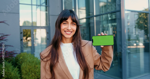 Fotografie Confident businesswoman in suit smiling and holding a smartphone with a green screen