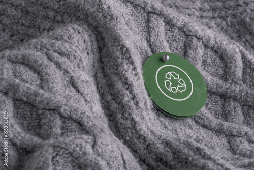 Foto A circular green tag with a recycling symbol hangs from on gray knitted fabric