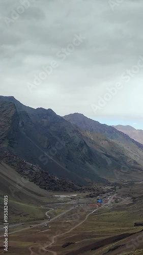 Vertical view of a massive dark rocky mountain with a hanging glacier and base camp.
