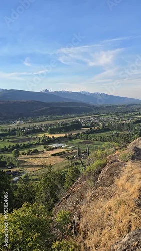 Vertical panning of a green mountain valley town surrounded by distant peaks.