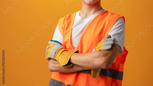 Worker poses with arms crossed in safety gear against orange background