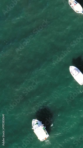 Top-down drone shot of small boats floating on clear turquoise water near Koroni, Greece. Peaceful maritime scene with vivid colors and gentle waves.