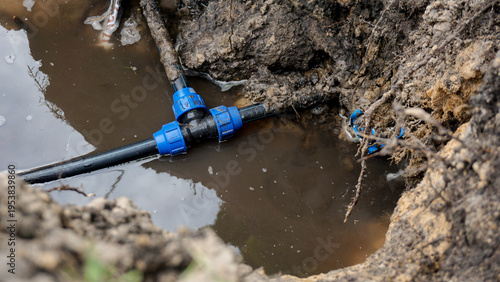 Underground water pipe with blue plastic compression fittings submerged in muddy flooded excavation pit, water leak repair, plumbing emergency, or utility infrastructure maintenance