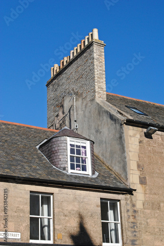 Old Stone Building with Dormer Window and Chimney Stack seen from Below against Blue Sky 