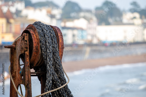 Canvastavla Rusting fishing winch on a British shingle beach with small boat, capturing a quiet coastal scene in a traditional fishing town