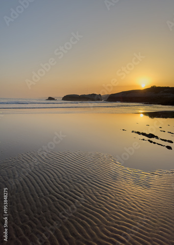 Golden sunrise over calm Atlantic ocean with mirror reflection on wet beach sand minimal coastal landscape peaceful morning seascape Virgen del Mar Cantabria Spain