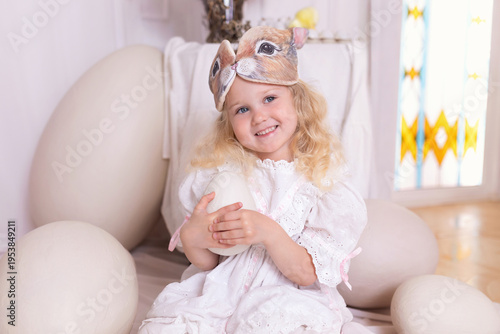 Wallpaper Mural A little blonde girl in a white dress and a rabbit ears mask on the head is smiling sit with with large Easter eggs. Happy child girl with bunny ears holding an easter egg in her hands. Vintage style Torontodigital.ca