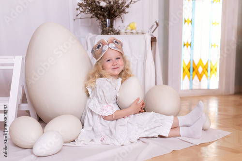 Wallpaper Mural A little blonde girl in a white dress and a rabbit ears mask on the head is smiling sit with with large Easter eggs. Happy child girl with bunny ears holding an easter egg in her hands. Vintage style Torontodigital.ca