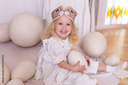Wallpaper Mural A little blonde girl in a white dress and a rabbit ears mask on the head is smiling sit with with large Easter eggs. Happy child girl with bunny ears holding an easter egg in her hands. Vintage style Torontodigital.ca