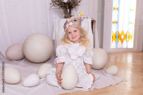 Wallpaper Mural A little blonde girl in a white dress and a rabbit ears mask on the head is smiling sit with with large Easter eggs. Happy child girl with bunny ears holding an easter egg in her hands. Vintage style Torontodigital.ca