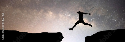 A person jumps between two cliffs, representing courage and risk-taking against the night sky