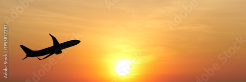 Silhouette of an airplane soaring against a warm, orange sunset sky