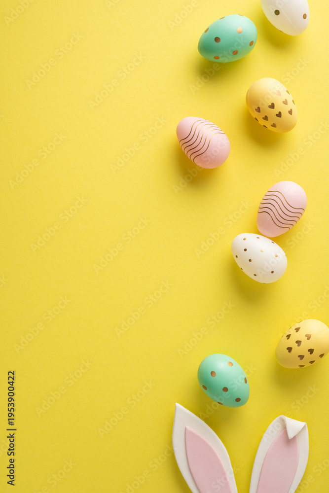 Obraz premium Happy Easter vertical greeting featuring pastel decorated egg and bunny ear on a bright yellow background ideal for spring holiday designs