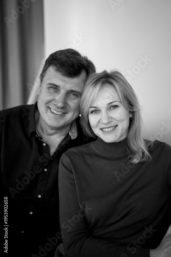 attractive middle-aged married couple hugging and smiling on sofa, studio photo shoot